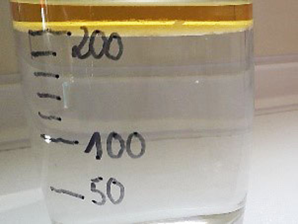 Das Bild zeigt ein transparentes Gef&auml;&szlig; mit einer Fl&uuml;ssigkeit, das von au&szlig;en beschriftet ist. An den Seiten sind Messskalen mit den Werten 50, 100 und 200 markiert, die wahrscheinlich Milliliter anzeigen.