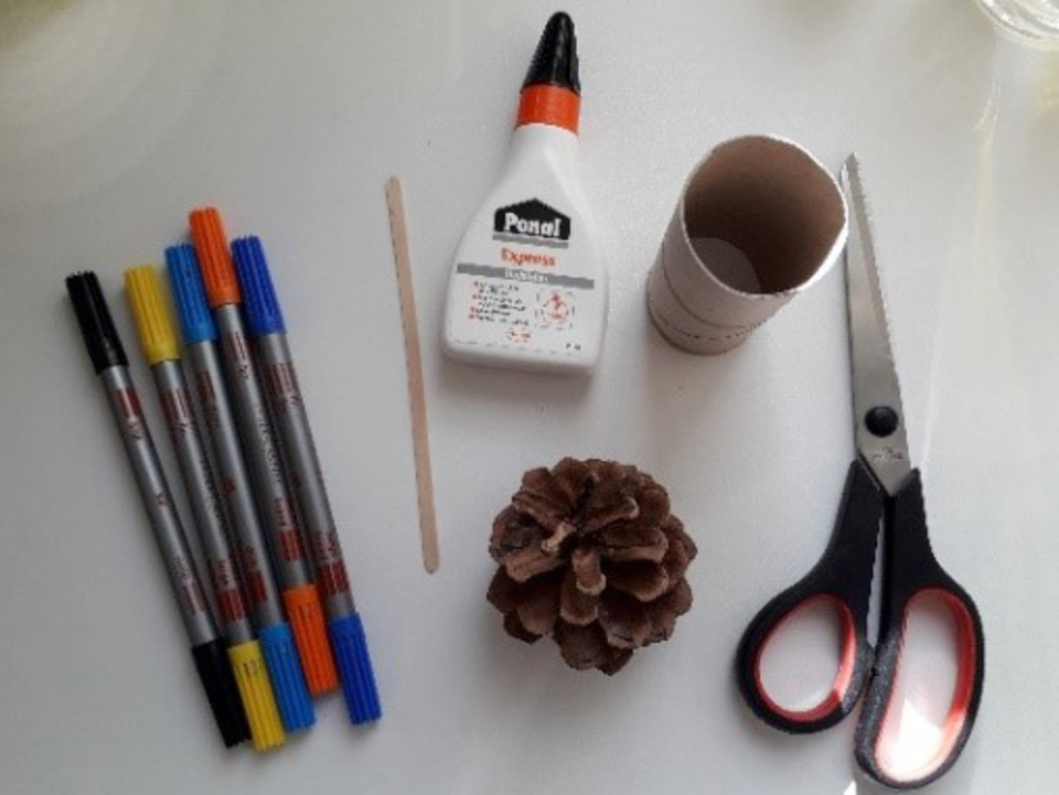 Das Bild zeigt eine Sammlung von Bastelmaterialien, darunter bunte Filzstifte, eine Flasche Kleber, eine Schere, einen Bastelholzstab und eine Kiefernnuss. Au&szlig;erdem ist ein Papprollk&ouml;rper abgebildet, der f&uuml;r kreative Projekte genutzt werden kann.