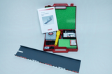 Das Bild zeigt eine rote Box mit dem Titel „Mini-Box Elementarphysik-Optik“, die verschiedene Experimentiermaterialien enthält, darunter eine Taschenlampe und weitere Zubehörteile. Neben der Box liegt eine schwarze Schiene, die wahrscheinlich Teil des Exp