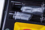 Das Bild zeigt ein Set bestehend aus transparenten Spritzen und Reagenzgläsern, die sorgfältig in einem gepolsterten Koffer angeordnet sind. Zusätzlich sind ein gelbes Behältnis und ein rotes Element sichtbar, die Teil des Experimentierbedarfs sind.