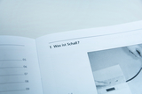 Das Bild zeigt eine offene Seite eines Buches mit der Überschrift „Was ist Schall?“. Außerdem ist eine Illustration zu sehen, die vermutlich mit dem Experimentieren von Schallphänomenen zusammenhängt.