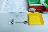 Das Bild zeigt ein Experimentier-Set zum Thema "Schwimmen und Sinken", das verschiedene Materialien wie Kugeln und Messbecher enthält. Außerdem sind eine Anleitung und ein gelbes Behältnis sichtbar, die für praktische Experimente im Bildungswesen verwende