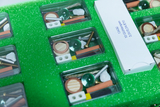 Das Bild zeigt ein Set mit Experimentiermaterialien, das in einem grünen, gepolsterten Koffer organisiert ist. Es enthält verschiedene Komponenten wie Glühbirnen, Schrauben und kleine Objekte für experimentelle Zwecke im Bildungsbereich.