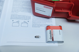 Das Bild zeigt ein Experimentier-Set für Stromkreise von Cornelsen, das eine Batterie und eine Glühbirne umfasst. Daneben liegt eine Anleitung, die verschiedene Verbindungsmöglichkeiten und Versuche beschreibt.