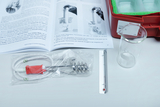 Das Bild zeigt ein Experimentier-Set mit einem Thermometer, einem Heizgerät mit Spirale, einem Glasgefäß und einer Anleitung. Diese Materialien sind für Experimente im Bildungsbereich vorgesehen und sollen den Schülern helfen, Thermodynamik zu verstehen.