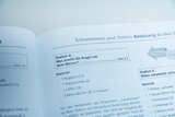 Das Bild zeigt eine Anleitung für ein Experiment im Bereich "Schwimmen und Sinken". Es beschreibt Station 4, die Fragen zur Interaktion einer Kugel mit Wasser behandelt, und listet dazu benötigtes Material auf.