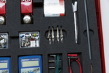 Das Bild zeigt eine kompakte Sammlung von Experimentiermaterialien, die in einem gepolsterten Koffer organisiert sind. Enthalten sind unter anderem Messgeräte, Glühlampen, Batterien und verschiedene Verbindungselemente, die für Bildungszwecke genutzt werd