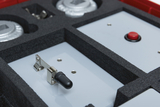 Das Bild zeigt einen Ausschnitt aus einem Experimentier-Kit, das verschiedene elektrische Komponenten enthält, darunter Schalter und Tasten. Die Teile sind ordentlich in einem Schaumstoffeinlage aufbewahrt, die eine sichere Lagerung und einfache Handhabun