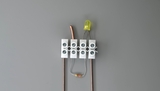 Das Bild zeigt eine einfache Schaltung mit einer LED, einem Widerstand und Verbindungsdrähten. Diese Komponenten sind auf einem grauen Untergrund angeordnet und dienen dem Experimentieren mit elektrischen Stromkreisen.