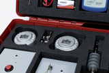 Das Bild zeigt ein Set für experimentelle Anwendungen, das in einem roten Koffer untergebracht ist. Im Inneren befinden sich mehrere Bauteile, darunter zwei metallische Objekte, Verbindungskabel, eine Batterie und ein Messgerät, alles in passgenauer Schau
