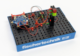 Das Bild zeigt ein Aufbau-Set von fischertechnik, das aus einer robusten Plattform mit Drähten und elektronischen Komponenten besteht. Diese Teile sind für Experimente im Bereich Technik und Informatik im Bildungswesen konzipiert.