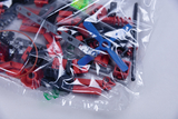 Das Bild zeigt eine durchsichtige Plastiktüte, die mit bunten Experimentierbauteilen gefüllt ist, darunter rote, schwarze und grüne Teile sowie ein blaues Propellerstück. Diese Materialien sind wahrscheinlich für den Einsatz im Bildungsbereich gedacht, um