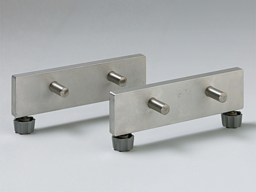 Das Bild zeigt zwei metallische Teile, die parallel zueinander angeordnet sind. Jedes Teil hat mehrere Stifte und ist auf einem stabilen Untergrund mit verstellbaren Füßen montiert, wahrscheinlich für physikalische Experimente.