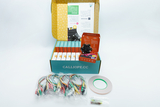Das Bild zeigt einen geöffneten Karton mit einem Experimentierkit, das einen Calliope mini Mikrocontroller und verschiedene Zubehörteile wie Kabel, Klebeband und Bauteile enthält. Dieses Set ist ideal für den Unterricht im deutschen Bildungswesen, um Programmier- und Elektronikkenntnisse zu vermitteln.
