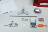 Auf dem Bild sind verschiedene Experimentiermaterialien zu sehen, darunter ein Reagenzglas, eine Waage, ein Stativ und eine Kerze. Diese Utensilien sind typischerweise für chemische Experimente im Bildungsbereich gedacht.