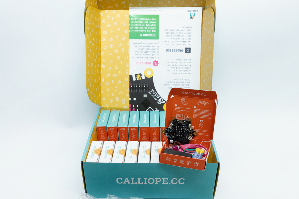 Das Bild zeigt eine offene Verpackung mit dem Calliope Mini, einem programmierbaren Mikrocontroller für den Bildungsbereich, umgeben von bunten Modulboxen. Inhaltsinformationen liegen ebenfalls prominent auf der Innenseite des Deckels.