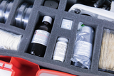 Das Bild zeigt ein Set mit Experimentiermaterialien, das in einer gepolsterten Box organisiert ist. Enthalten sind verschiedene chemische Substanzen wie Iod-Kaliumiodid-Lösung, D(+)-Glucose und ein Fläschchen mit pflanzlichem Öl, sowie Mikroskopabdeckgläser.
