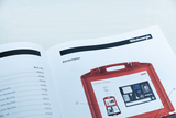 Das Bild zeigt eine Seite aus einem Katalog für Experimentiermaterialien, die einen Einräumplan für ein Set zur Windenergie darstellt. Auf der Abbildung ist ein roter Koffer abgebildet, der mit verschiedenen Experimentiermaterialien gefüllt ist.