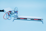 Das Bild zeigt ein Experimentiergerät, das einen Motor mit Propeller und eine Führungsschiene umfasst. Es dient zur Durchführung von Versuchen im Bereich Physik, insbesondere zur Veranschaulichung von Kräften und Bewegungen.
