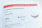 Das Bild zeigt eine Seite aus einem Experimentierbuch, die sich mit dem Thema Schall beschäftigt. Es listet die benötigten Materialien für einen Versuch auf, darunter Verschlüsse und ein Schlagzeuger, um Schall zu erzeugen.