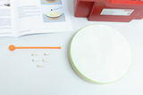 Das Bild zeigt eine Experimentierausstattung für den Bereich Licht und Schall, bestehend aus einer Trommel, einem orangefarbenen Stab und mehreren metallischen Klammern. Daneben liegt ein Handbuch, das Anleitungen für Experimente bietet.