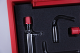Das Bild zeigt ein Set aus Glasgeräten, das in einer roten Schaumstoffeinlage geschützt ist. Die Geräte sind für chemische Experimente gedacht und beinhalten verschiedene Formen von Röhren und Flaschen mit roten Verschlüssen.