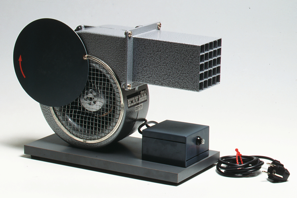 Das Bild zeigt ein Experimentiergerät in Form eines Ventilators mit einem runden Deckel und einem rechteckigen Auslass. Das Gerät wird mit einem Stromkabel betrieben und eignet sich für Bildungszwecke im Bereich Physik oder Technik.