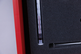 Das Bild zeigt ein Messgerät, wahrscheinlich ein Thermometer oder eine Graduierte Pipette, das in einem gepolsterten Schaumstoffeinleger liegt. Der rand von rot lackierten Material ist ebenfalls sichtbar, was auf eine sachgerechte Aufbewahrung im Experimentierbedarf hinweist.