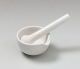 Das Bild zeigt ein weißes Porzellanmörser-Set, bestehend aus einer Schale mit einem passenden Stößel. Es wird häufig im Experimentierbedarf für chemische oder biologische Anwendungen verwendet.