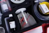 Das Bild zeigt ein Experimentier-Kit mit verschiedenen wissenschaftlichen Materialien, darunter eine Flasche mit einer chemischen Lösung, ein transparentes Gerät und mehrere Behälter. Die Komponenten sind ordentlich in einem Schaumstoffeinsatz angeordnet, um Sicherheit und Organisation zu gewährleisten.