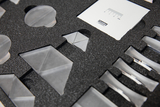 Das Bild zeigt eine Anordnung transparenter geometrischer Formen, die in einer strukturierten Schaumstoffeinlage platziert sind. Diese Materialien können für experimentelle Zwecke im Bildungswesen verwendet werden, um physikalische Konzepte zu veranschaulichen.