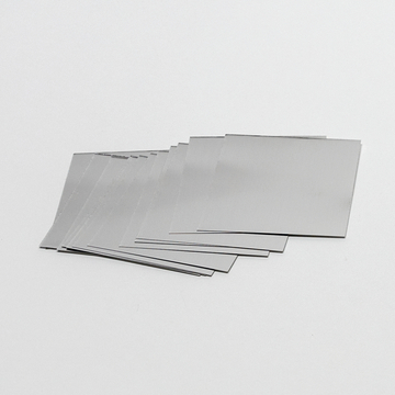 Das Bild zeigt eine Reihe von quadratischen, metallischen Platten, die auf einem weißen Untergrund liegen. Sie scheinen Teil eines Experimentierkits zu sein, das im Rahmen von Bildungszwecken verwendet wird.