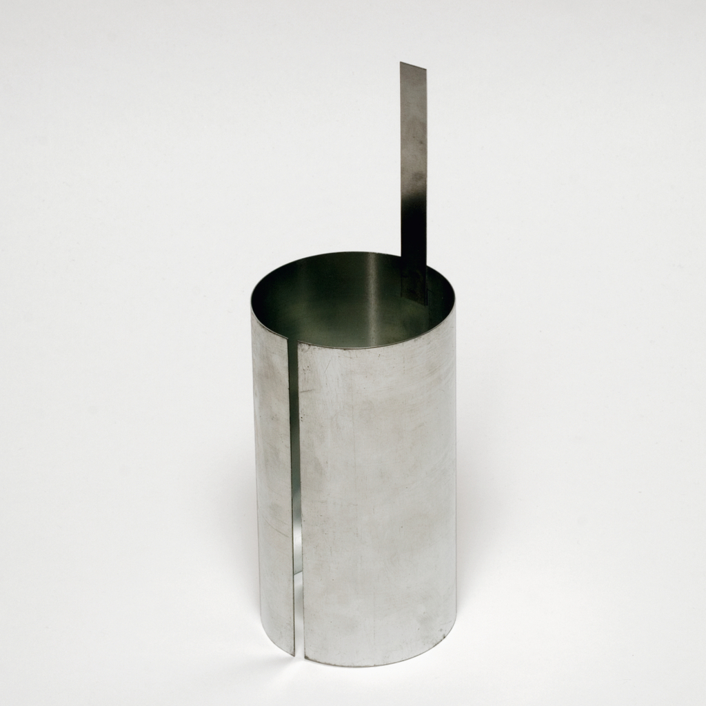 Das Bild zeigt einen zylindrischen Behälter aus Metall mit einer seitlichen Kerbe und einem vertikalen Metallstreifen, der aus dem oberen Rand herausragt. Dieses Experimentiergerät wird häufig im Bildungsbereich verwendet, um physikalische Konzepte zu demonstrieren.