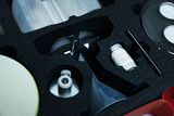 Das Bild zeigt eine Sammlung von Experimentiermaterialien, die in einem gepolsterten Koffer angeordnet sind. Zu den sichtbaren Gegenständen gehören Messbecher, eine Pipette, Chemikalien und Sicherheitsbrille, die für Unterrichtszwecke im naturwissenschaftlichen Bereich verwendet werden.