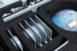Das Bild zeigt ein Set mit verschiedenen experimentellen Materialien, das in einer gepolsterten Box angeordnet ist. Zu sehen sind mehrere graue Scheiben und ein Globus, die für physikalische Experimente im Bildungsbereich verwendet werden können.