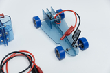 Das Bild zeigt einen transparenten, blauen Modellautokörper mit aufgesteckten Gummirädern und elektrischen Verbindungen. Daneben liegen mehrere Kabel, die für Experimente im Bildungsbereich verwendet werden können.