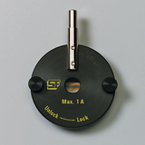 Das Bild zeigt ein schwarzes experimentelles Gerät mit einem Metallständer in der Mitte. Es ist mit der Aufschrift "Max. 1 A" und "Unlock" sowie "Lock" versehen, was auf eine Funktion zur Steuerung von elektrischen Strom hinweist.