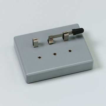 Das Bild zeigt ein graues Experimentiergerät mit zwei Metallkontakten und einem Schalter. Es dient wahrscheinlich zur Durchführung elektrischer Experimente im Bildungsbereich.
