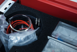 Das Bild zeigt einen Experimentierkasten, der verschiedene Utensilien enthält, darunter ein Glasgefäß und rote Kabel. Die Utensilien sind ordentlich in einer gepolsterten Box angeordnet, um sie bei Experimenten im Bildungswesen zu verwenden.