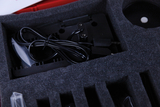 Das Bild zeigt eine gepolsterte Box mit verschiedenen Kabeln und einem elektrischen Bauteil. Die Komponenten sind ordentlich in Schaumstoff ausgelegt, was auf einen Schutzbedarf während des Transports hinweist.