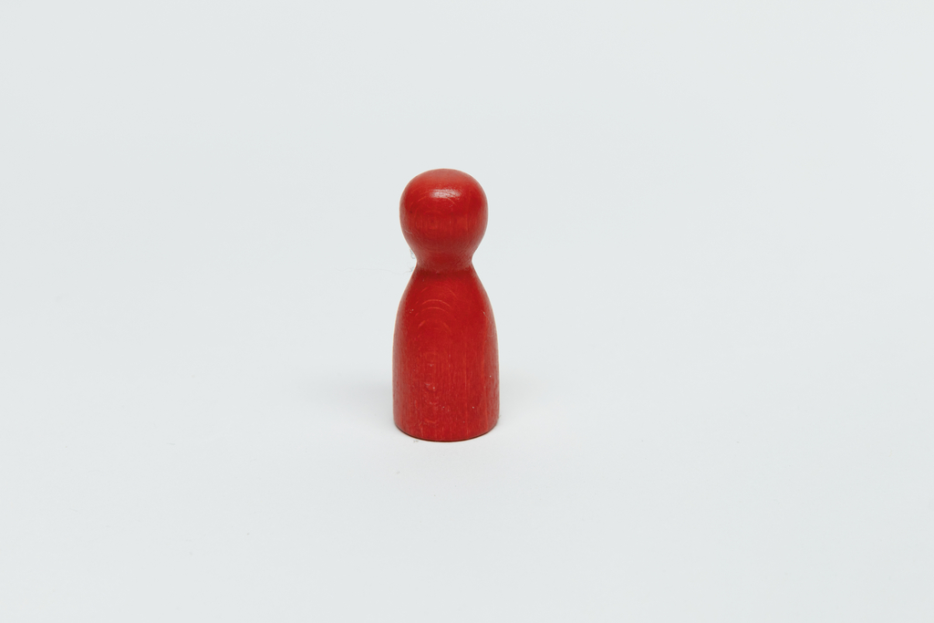 Das Bild zeigt eine rote Holzfigur, die die Form eines menschlichen Steckmännchens hat. Sie steht auf einem neutralen, weißen Hintergrund und eignet sich gut für den Einsatz im Bildungsbereich, beispielsweise für Experimentier- oder Gruppenspiele.