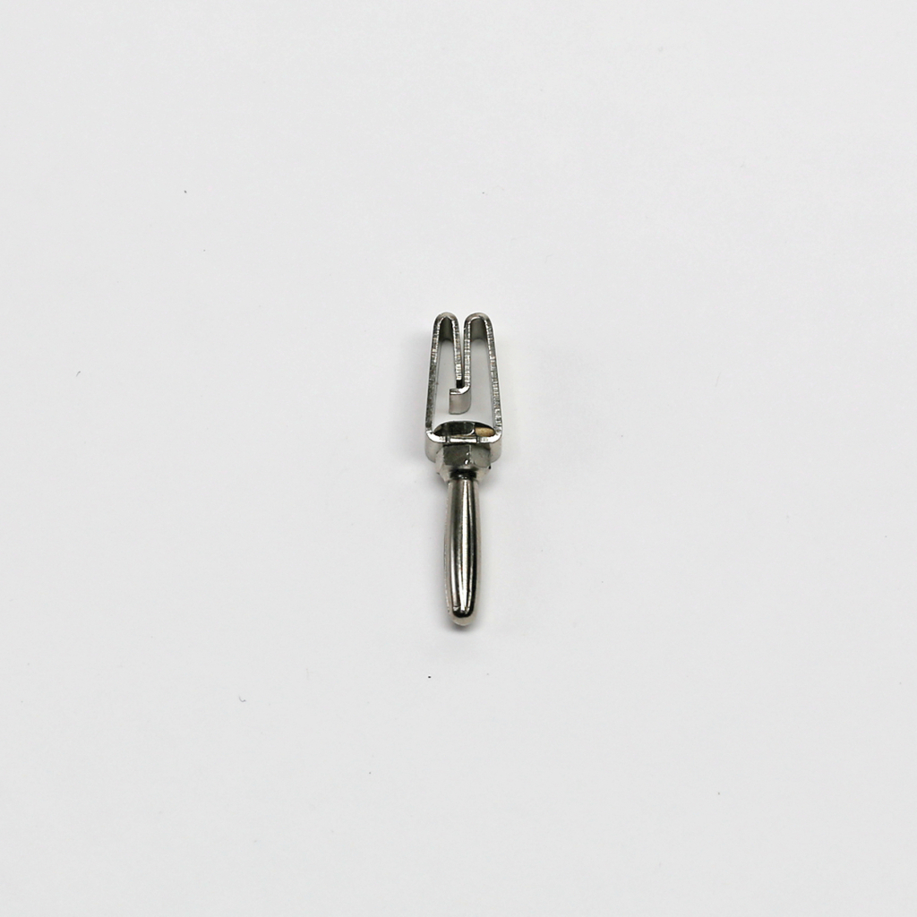 Das Bild zeigt eine kleine, metallische Gabel mit zwei prongartigen Spitzen, die typischerweise für wissenschaftliche Experimente oder zur Demonstration physikalischer Konzepte verwendet wird. Sie ist auf einem weißen Hintergrund platziert, was den Fokus auf das Werkzeug legt.