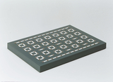 Das Bild zeigt eine graue Plattform mit einer Anordnung von metallenen Kontakten in rechteckiger Form. Diese Struktur könnte für Experimente im Bereich Elektronik oder Physik verwendet werden, um Stromkreise zu erstellen oder zu untersuchen.