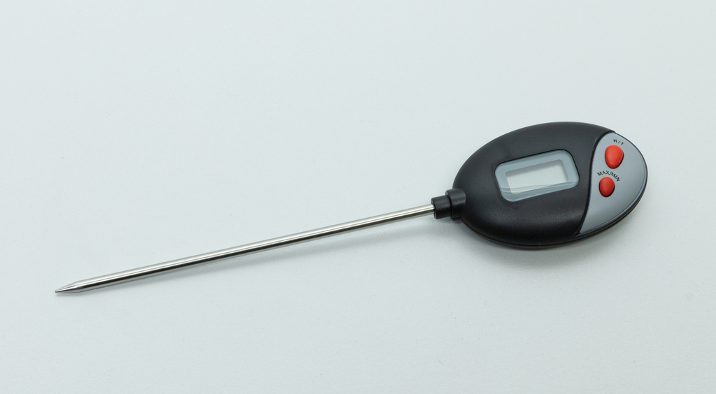 Das Bild zeigt ein digitales Thermometer mit einer langen metallen Spitze und einem ovalen Gehäuse in schwarz und grau. Es verfügt über eine LCD-Anzeige sowie zwei rote Tasten zur Bedienung, vermutlich für Funktionen wie MAX/MIN und HOLD.