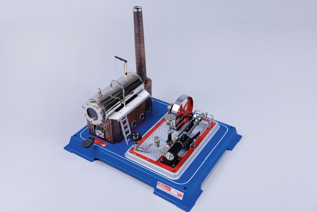 Das Bild zeigt eine Modell-Dampfmaschine, die aus einem Kessel und einer rotierenden Maschine besteht. Sie ist auf einer blauen Plattform montiert und dient zu Experimentierzwecken im Bildungsbereich.
