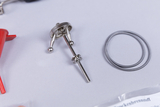 Das Bild zeigt verschiedene Studienmaterialien, darunter ein metallisches Gerät mit Kugeln und eine rote Kunststoffkomponente, sowie zwei Drahtschlingen. Diese Elemente sind Teil eines Experimentsatzes für das Bildungswesen in Deutschland.