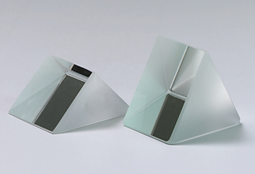 Das Bild zeigt zwei prismatische Glasobjekte, die leicht geneigt stehen. Sie sind jeweils halbdurchsichtig und haben eine flache, schwarze Fläche an der Seite, die für optische Experimente genutzt werden kann.