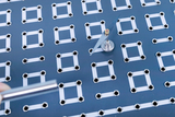 Das Bild zeigt eine experimentelle Plattform mit einer Struktur aus silbernen Ringen und weißen Linien, auf der sich ein kreisförmiges Gerät mit einem rotierenden Element befindet. Ein glänzender Metallstab wird zur Manipulation des Experiments in der Nähe gehalten.