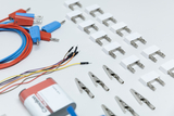 Das Bild zeigt verschiedene elektrische Verbindungselemente, darunter Kabel mit farbigen Steckerenden, Klemmen und Adapter. Diese Produkte sind für den Einsatz in Experimenten im Bildungsbereich konzipiert und dienen zur sicheren Verbindung von elektrischen Bauteilen.