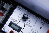 Das Bild zeigt ein elektrisches Experimentiergerät mit einem Regel- und Anzeigepanel. Zu sehen sind Einstellknöpfe für Widerstand und Strom sowie Anschlüsse für unterschiedliche Lasten wie Lampen oder Motoren.